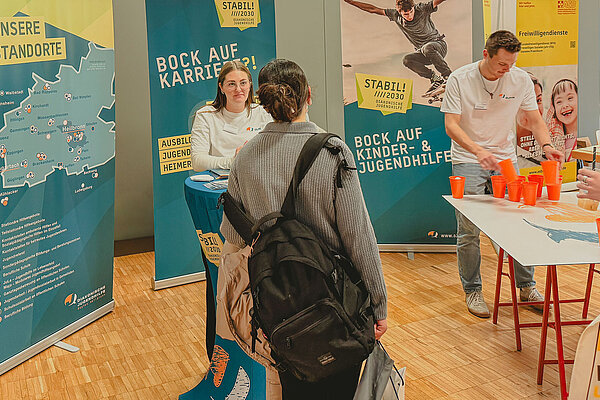 Zwei DJHN Mitarbeitende am Stand der Ausbildungsmesse unterhalten sich mit einer Jugendliche, die sich für die Arbeit in der DJHN interessiert.
