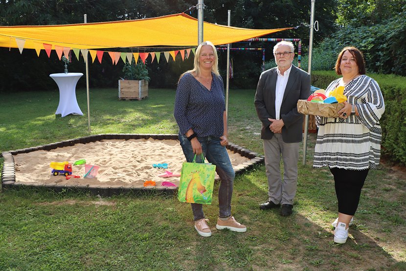 Gemeinderatsvorsitzender Dieter Barthruff überreicht an DJHN-Fachbereichsleiterin Ute Thumer (links) und an Teamleiterin der Wohngruppe Anja Schädler (rechts) vor dem neuen zertifizierten Sandkasten ein kleines Geschenk.